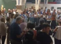 Pubblico in piedi tra archi in pietra e quadri appesi a pannelli bianchi alla mostra del Collettivo BAI a Comiso