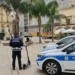 Agente della Polizia Locale di spalle accanto a un monopattino elettrico in una piazza di Comiso, vicino a un’auto di servizio