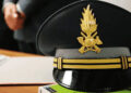 Berretto d’ordinanza della Guardia di Finanza con fregio dorato, appoggiato su una scrivania accanto a fogli e un libro