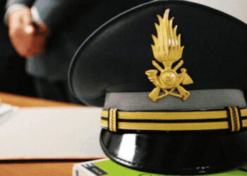 Berretto d’ordinanza della Guardia di Finanza con fregio dorato, appoggiato su una scrivania accanto a fogli e un libro