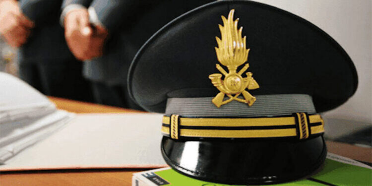 Berretto d’ordinanza della Guardia di Finanza con fregio dorato, appoggiato su una scrivania accanto a fogli e un libro