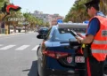 Carabiniere con etilometro accanto a un’auto di servizio durante i controlli dei carabinieri su un viale alberato