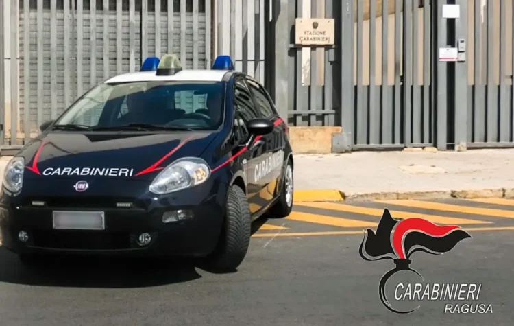 Auto dei carabinieri con lampeggianti blu parcheggiata davanti al cancello di una stazione, con il logo Carabinieri Ragusa