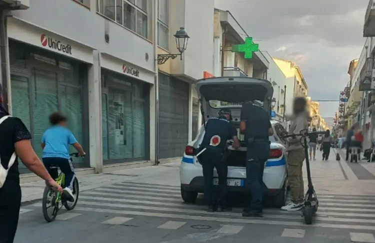 Agenti della polizia locale di Vittoria in controllo accanto all'auto di servizio, vicino a un uomo con un monopattino elettrico