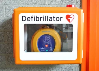 Defibrillatore semiautomatico giallo in una teca arancione fissata a un muro di mattoni grigi, con il simbolo del cuore rosso