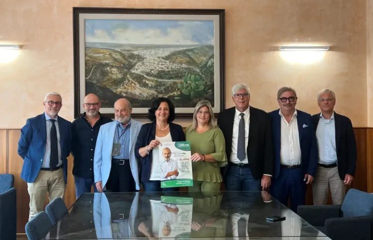 Otto persone in posa in una sala istituzionale di Ragusa mostrano il manifesto sulla donazione degli organi con il QR Code