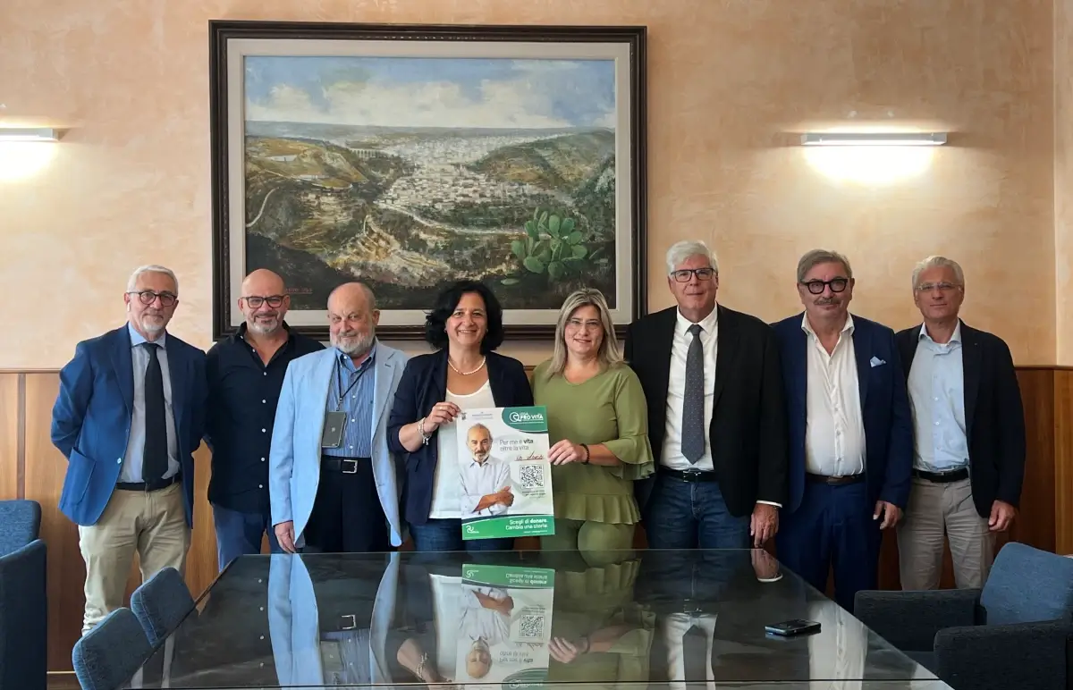 Otto persone in posa in una sala istituzionale di Ragusa mostrano il manifesto sulla donazione degli organi con il QR Code