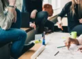 Donne sedute attorno a un tavolo che scrivono con matite colorate su grandi fogli di carta durante un lavoro di gruppo