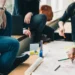 Donne sedute attorno a un tavolo che scrivono con matite colorate su grandi fogli di carta durante un lavoro di gruppo