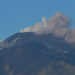 Pennacchio vulcanico grigio e rosato si alza dalla cima innevata dell’Etna e si allunga verso destra sotto un cielo azzurro