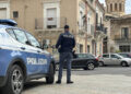 Agente della Polizia di Stato di spalle accanto a un’auto di servizio, in una piazza con palazzi storici e una cupola