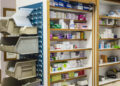 Scaffali in legno di una farmacia con scatole di farmaci ordinate per ripiano e contenitori grigi per i medicinali