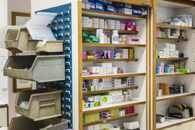 Scaffali in legno di una farmacia con scatole di farmaci ordinate per ripiano e contenitori grigi per i medicinali