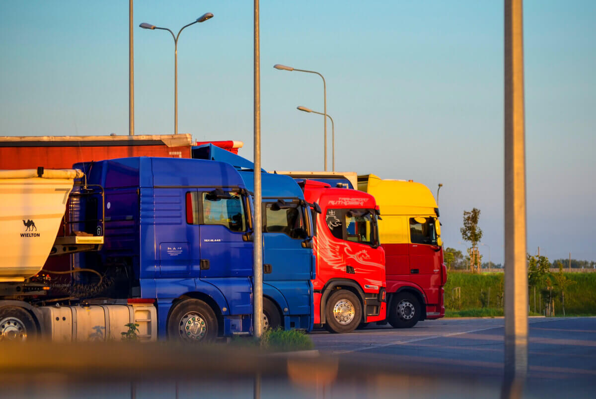 Camion dell’autotrasporto fermi in fila in un piazzale al tramonto, con motrici blu, rosse e gialle