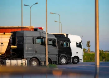 Tir fermi uno accanto all’altro in un piazzale di sosta al tramonto, con motrici grigie, nera e bianca