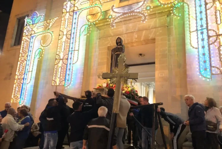 Fedeli portano il simulacro di San Francesco fuori dalla chiesa illuminata a festa durante la processione a Ragusa