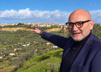Il geologo Filippo Cappotto con occhiali e giacca blu indica un paese su una collina tra uliveti e prati verdi