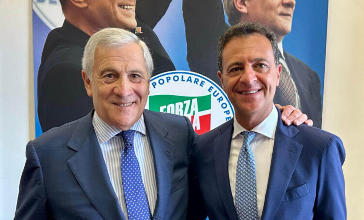 Antonio Tajani e Nino Minardo sorridenti, abbracciati davanti a un manifesto con il logo di Forza Italia