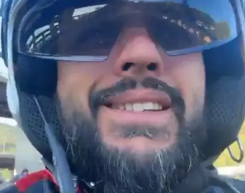 Francesco Nicolosi sorride con casco bianco e occhiali da sole a specchio, inquadrato dal basso durante un giro in scooter