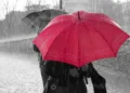 Maltempo, due persone sotto la pioggia battente con un ombrello rosso e uno scuro su una strada lastricata