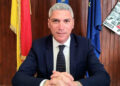 Peppe Dimartino, sindaco di Santa Croce Camerina, seduto alla scrivania con le bandiere di Sicilia, Italia e Unione europea