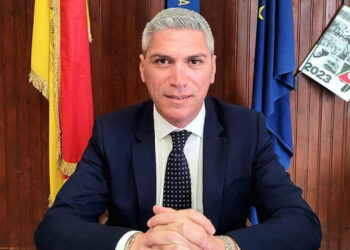 Peppe Dimartino, sindaco di Santa Croce Camerina, seduto alla scrivania con le bandiere di Sicilia, Italia e Unione europea