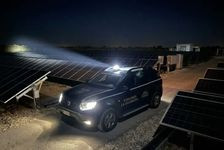 Auto della vigilanza La Sicurezza con il lampeggiante acceso tra i pannelli di un impianto fotovoltaico di notte