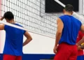 Giocatori del Giarratana Volley in maglia blu e pantaloncini rossi, di spalle sotto la rete durante un allenamento in palestra