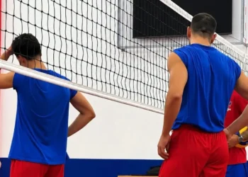 Giocatori del Giarratana Volley in maglia blu e pantaloncini rossi, di spalle sotto la rete durante un allenamento in palestra