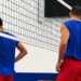 Giocatori del Giarratana Volley in maglia blu e pantaloncini rossi, di spalle sotto la rete durante un allenamento in palestra
