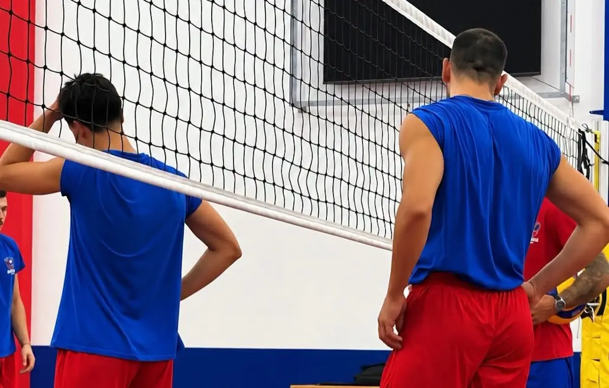 Giocatori del Giarratana Volley in maglia blu e pantaloncini rossi, di spalle sotto la rete durante un allenamento in palestra