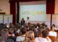 Studenti in un'aula magna seguono la lezione di Green Game, con i pannelli della raccolta differenziata ai lati del palco