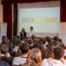 Studenti in un'aula magna seguono la lezione di Green Game, con i pannelli della raccolta differenziata ai lati del palco