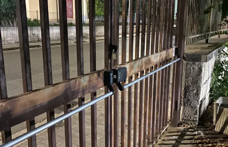 Cancello di un impianto sportivo a Ragusa con maniglione antipanico e lucchetto, affacciato su marciapiede e strada