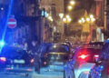 Incidente a Scicli: auto in coda di sera in una via del centro, con un lampeggiante blu e una statua su colonna illuminata