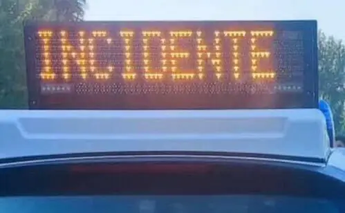 Pannello luminoso arancione con la scritta INCIDENTE sul tetto di un’auto della polizia, con lampeggiante blu