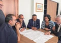 Sei persone attorno a un tavolo esaminano una mappa delle strade regionali tra Ragusa e Scicli in un ufficio con bandiere