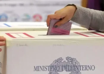 Una mano inserisce una scheda elettorale rosa in un’urna di cartone con il logo del Ministero dell’Interno