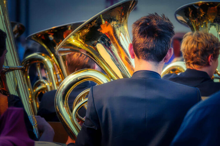 Giovani musicisti in giacca scura suonano tube ed eufonio, ripresi di spalle durante un concerto all’aperto