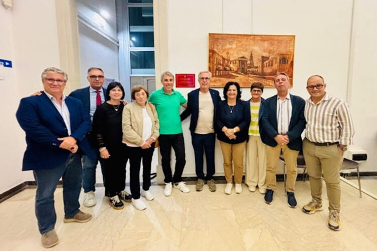 Dieci persone in posa in un atrio del Municipio di Comiso, ai lati della targa rossa in ricordo di Lino Rimmaudo