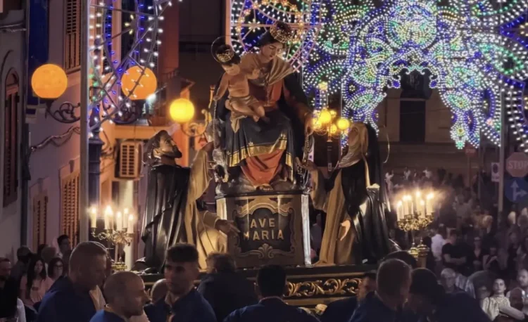Il simulacro della Madonna del Rosario in processione a Pozzallo tra luminarie, candelabri accesi e portatori in divisa blu
