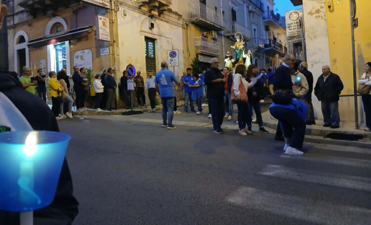 Fedeli lungo una via di Ragusa al passaggio della statua della Madonna del Rosario, con una candela accesa in primo piano