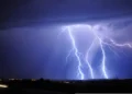 Fulmini durante un temporale notturno di maltempo, sotto un cielo viola, con le luci di un centro abitato all’orizzonte