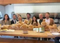 Otto persone dietro un bancone con pagnotte di pane e un cestino di mandorle, davanti a un forno a legna