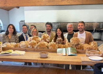 Otto persone dietro un bancone con pagnotte di pane e un cestino di mandorle, davanti a un forno a legna