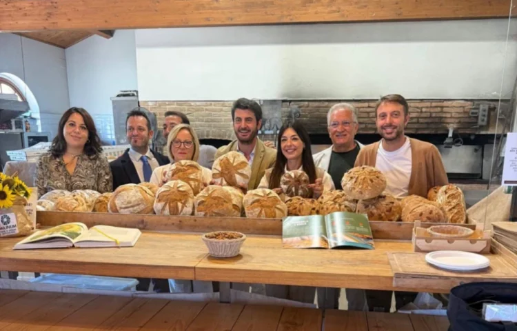 Otto persone dietro un bancone con pagnotte di pane e un cestino di mandorle, davanti a un forno a legna