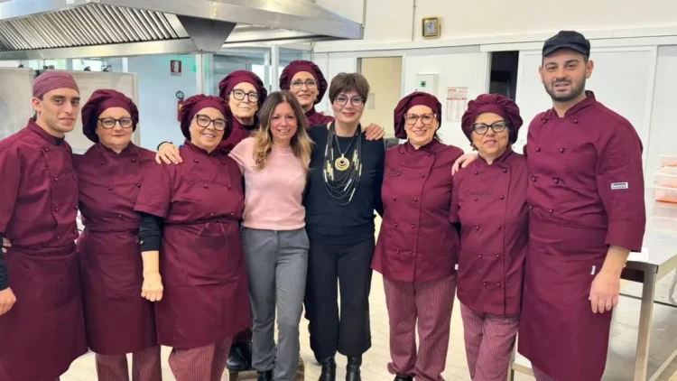 Personale della mensa scolastica in divisa bordeaux posa con due donne nella cucina comunale