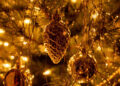 Pigna dorata e palline lucide tra fili d’oro e luci calde su un albero di Natale