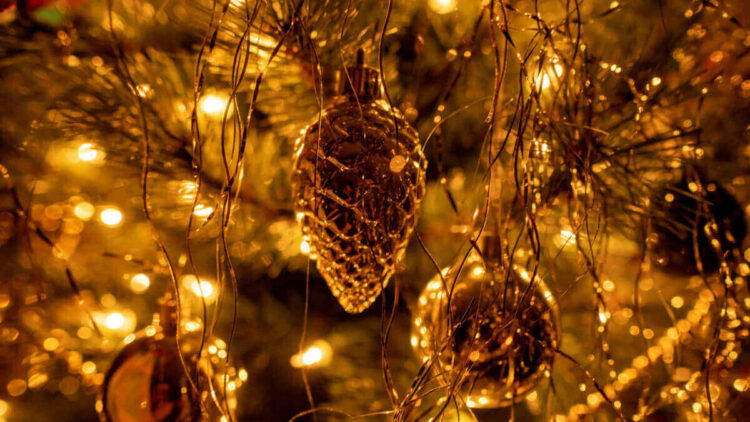 Pigna dorata e palline lucide tra fili d’oro e luci calde su un albero di Natale