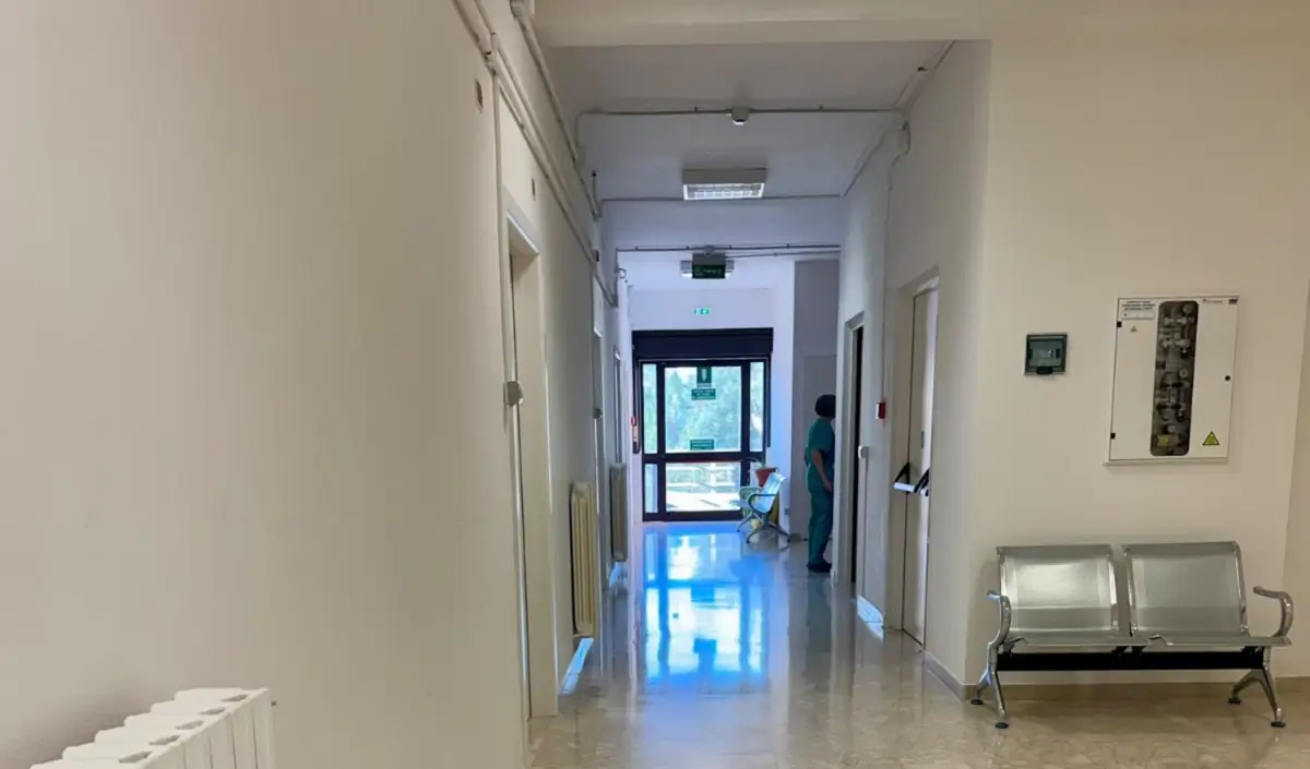 Corridoio del Pronto Soccorso di Modica con pavimento in marmo, panche in metallo e un'operatrice sanitaria in divisa verde